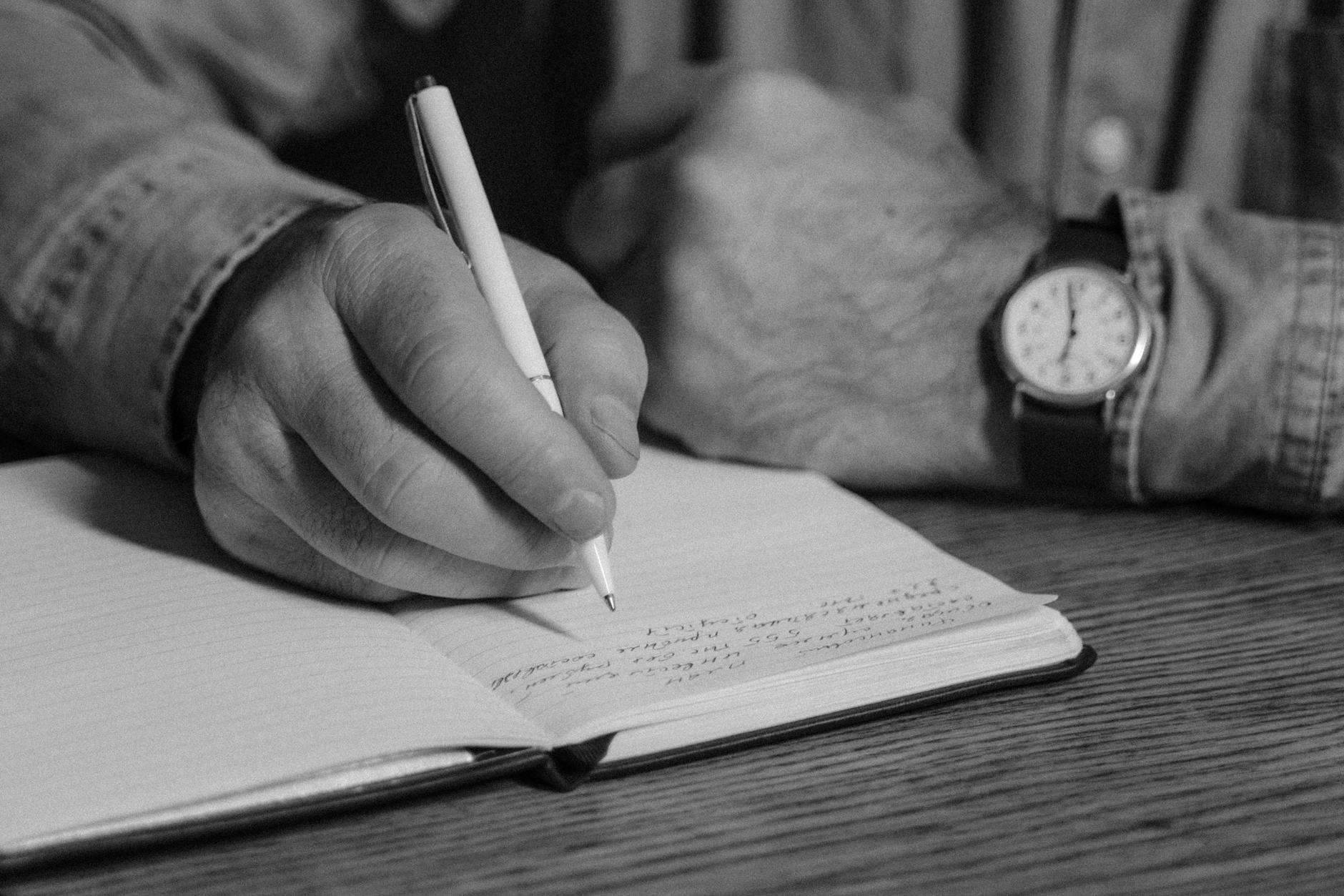 monochrome photo of person writing on a journal