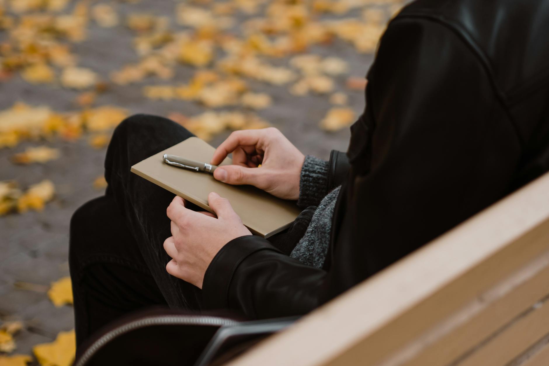 a person holding a notebook and pen sitting on a wooden bench