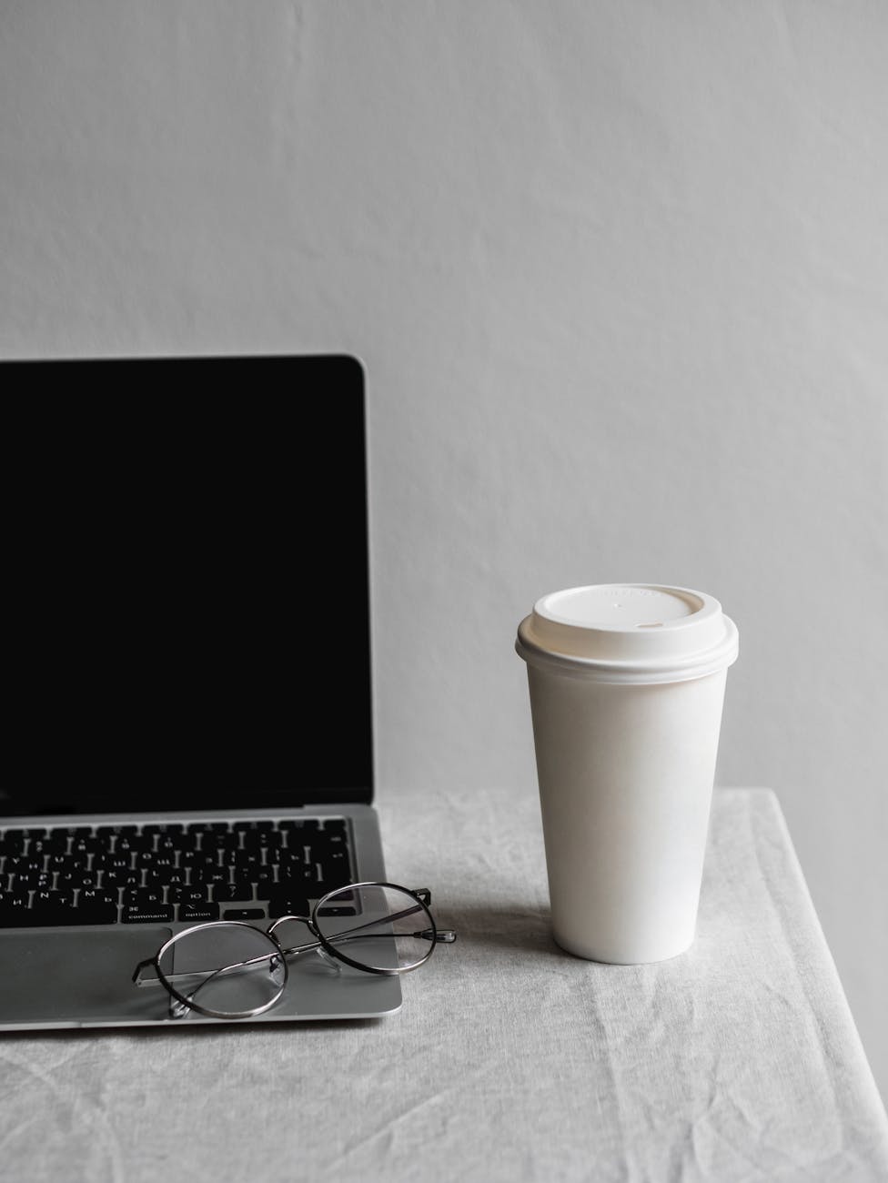disposable cup near eyeglasses and laptop